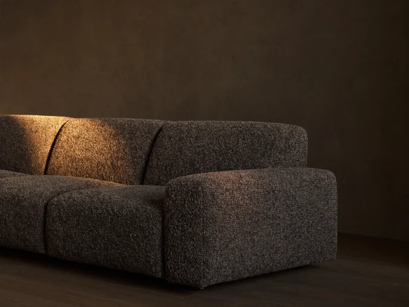 Anthrazitfarbenes Bouclé-Sofa im Dreiviertelwinkel vor dunkler Putzwand